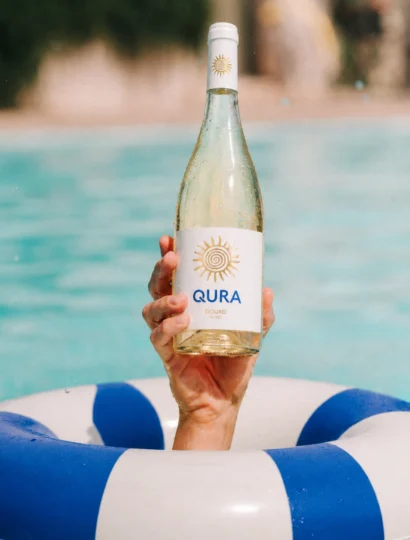 Botelha de vinho branco Qura à superfície de uma piscina, com um salva-vidas ao fundo